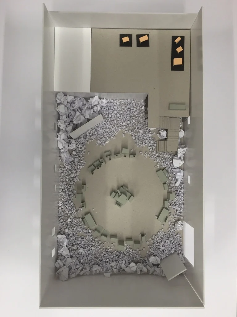 De maquette van de installatie: een cirkel van bureaus in een zee van papier.