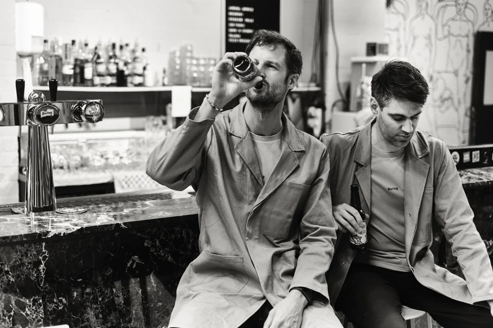 Remi Versteeg en Stijn de Weerd in grijze jassen aan de bar van hun studio